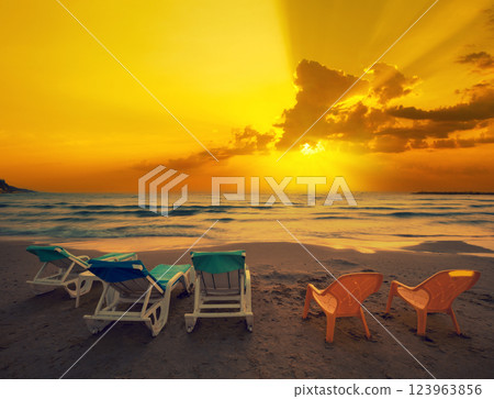 Seascape in the evening. Beach with chaise lounges at golden sunset Seascape in the evening. Beach with chaise lounges at golden sunset 123963856