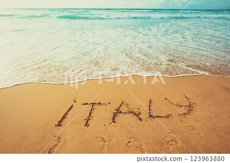 The inscription of Italy on the beach of white sand. Gradient color. 123963880