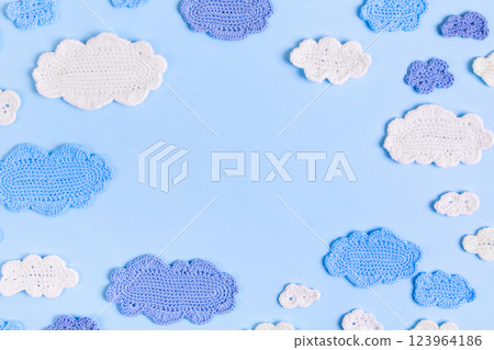 Knitted toys blue and white clouds on blue background with space for text. Baby stuff and accessories. Abstract knitted summer background. Top view, flat lay, copy space Knitted toys blue and white clouds on blue background with space for text. Baby stuff and accessories. Abstract knitted summer background. Top view, flat lay, copy space 123964186