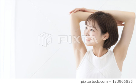 A woman stretching with her arms raised up. She is wearing a white tank top, isolated on a white background. Copy space. A woman stretching with her arms raised up. She is wearing a white tank top, isolated on a white background. Copy space. 123965855