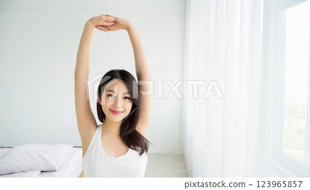 A woman stretching with her arms raised up. She is wearing a white tank top, isolated on a white background. Copy space. 123965857