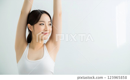 A woman stretching with her arms raised up. She is wearing a white tank top, isolated on a white background. Copy space. 123965858