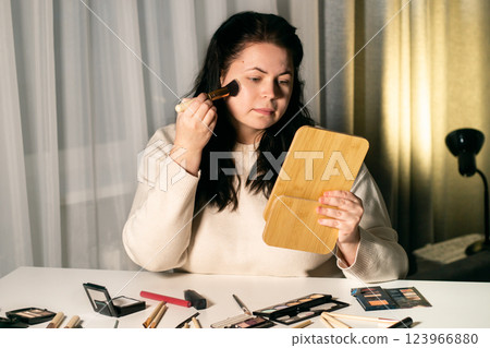 Woman applying face tone cream and looking in mirror at home. Putting on make-up with brush. Self make up. Woman applying face tone cream and looking in mirror at home. Putting on make-up with brush. Self make up. 123966880