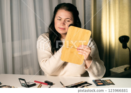 Woman doing make up looking in mirror at home. Putting on make-up with brush. Applying blush to face. Reflection in mirror. Woman doing make up looking in mirror at home. Putting on make-up with brush. Applying blush to face. Reflection in mirror. 123966881