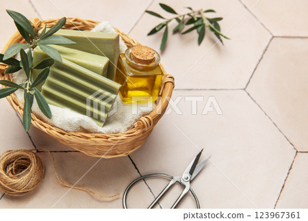 Olive soap bars, essential oil and scissors resting in wicker basket on tiled surface Olive soap bars, essential oil and scissors resting in wicker basket on tiled surface 123967361