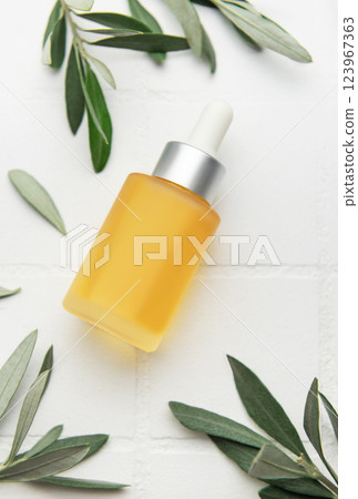 Natural cosmetic serum bottle with dropper surrounded by olive tree leaves on white tile background Natural cosmetic serum bottle with dropper surrounded by olive tree leaves on white tile background 123967363