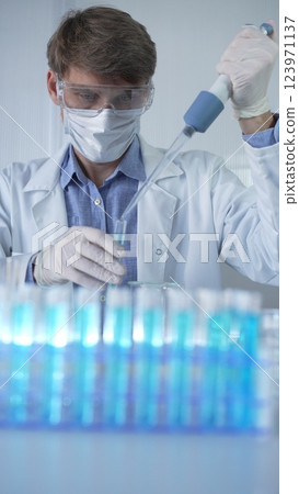Male scientist researcher, wearing lab coat, white medical gloves, mask and protective glasses is using micropipette filling test tubes in modern laboratory. Low key lighting. Science concept 123971137
