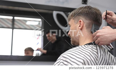 Professional barber trimming male client's hair using electric razor, creating precise haircut in barbershop setting with sleek styling tools 123971278