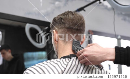 Professional hairstylist trimming client's hair using electric clippers, creating sleek, contemporary haircut with expert technique in modern barbershop setting 123971316