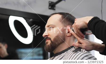 Skilled barber carefully grooming client's beard with electric razor, creating precise, trendy look inside contemporary barbershop setting Skilled barber carefully grooming client's beard with electric razor, creating precise, trendy look inside contemporary barbershop setting 123971325