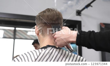 Professional hairstylist trimming client's hair using electric clippers, creating sleek, contemporary haircut with expert technique in modern barbershop setting 123971344