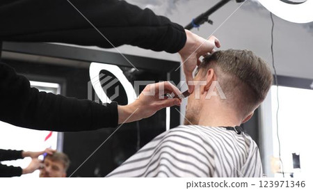 Skilled barber performing precise hair fade using straight razor, working on client's hair in contemporary grooming salon with professional tools 123971346