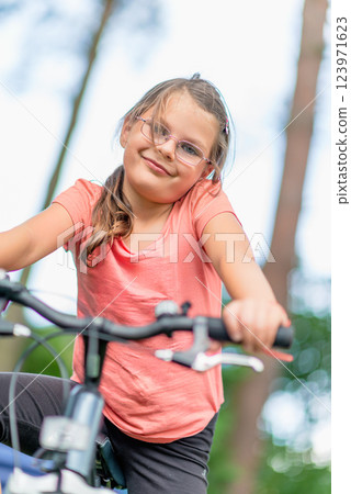 Young girl with glasses riding a bicycle outdoors in a green park, enjoying an active lifestyle and summer leisure time Young girl with glasses riding a bicycle outdoors in a green park, enjoying an active lifestyle and summer leisure time 123971623