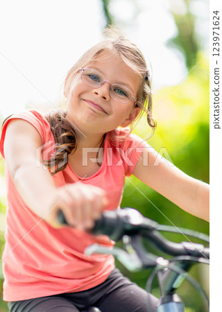 Young girl with glasses riding a bicycle outdoors in a green park, enjoying an active lifestyle and summer leisure time Young girl with glasses riding a bicycle outdoors in a green park, enjoying an active lifestyle and summer leisure time 123971624