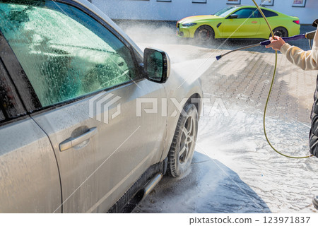 Washing an SUV with high-pressure water and foam at a self-service car wash, cleaning the vehicle exterior on a sunny day 123971837