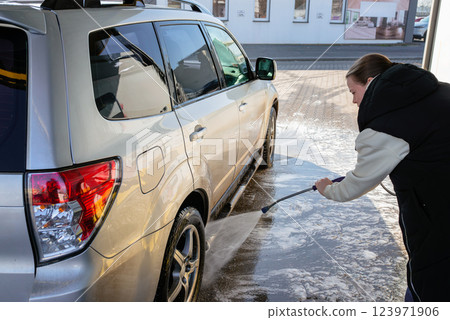 Woman Using High-Pressure Washer to Clean a Dirty SUV at a Self-Service Car Wash 123971906