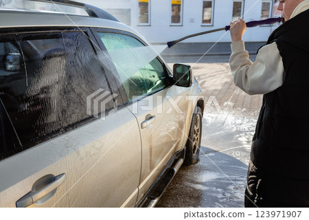 Woman Using High-Pressure Washer to Clean a Dirty SUV at a Self-Service Car Wash 123971907