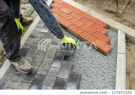 Construction worker laying gray concrete paving stones on gravel 123972582