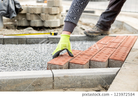 Construction worker placing red concrete paving stones in gravel bed during sidewalk construction 123972584