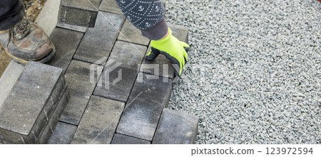 Construction worker laying paving stones on gravel in a residential area Construction worker laying paving stones on gravel in a residential area 123972594