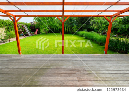 Wooden pergola with transparent polycarbonate roof covering a garden deck in a modern backyard Wooden pergola with transparent polycarbonate roof covering a garden deck in a modern backyard 123972684