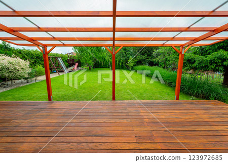 Wooden pergola with transparent polycarbonate roof covering a garden deck in a modern backyard 123972685