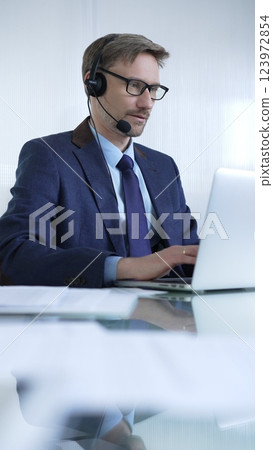 Businessman in blue suit is using a headset and laptop to offer customer service or online consultations. Business people concept 123972854