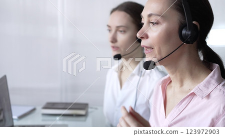 Focused female call center operator in pink casual blouse is assisting clients online, providing customer support and answering inquiries. Business call center Focused female call center operator in pink casual blouse is assisting clients online, providing customer support and answering inquiries. Business call center 123972903