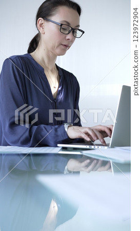 Focused businesswoman with glasses typing on laptop at modern glass desk in well lit office. Business people concept Focused businesswoman with glasses typing on laptop at modern glass desk in well lit office. Business people concept 123972904