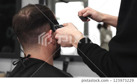 Skilled barber trimming client's hair using electric razor, creating contemporary hairstyle in modern barbershop setting with precise, professional technique Skilled barber trimming client's hair using electric razor, creating contemporary hairstyle in modern barbershop setting with precise, professional technique 123973229