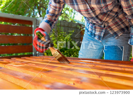 Close-up of a worker's gloved hand painting a wooden surface with a brush 123973900