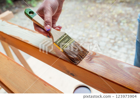 Close-up of a worker's hand applying wood stain with a paintbrush on wooden beams Close-up of a worker's hand applying wood stain with a paintbrush on wooden beams 123973904