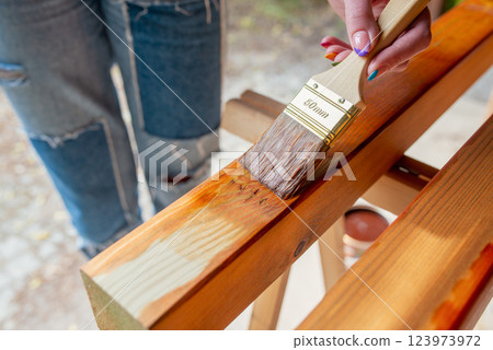 Close-up of a worker's hand applying wood stain with a paintbrush on wooden beams Close-up of a worker's hand applying wood stain with a paintbrush on wooden beams 123973972