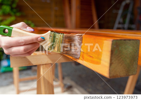 Close-up of a worker's hand applying wood stain with a paintbrush on wooden beams 123973973