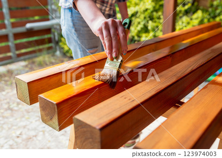 Close-up of a worker's hand applying wood stain with a paintbrush on wooden beams Close-up of a worker's hand applying wood stain with a paintbrush on wooden beams 123974003