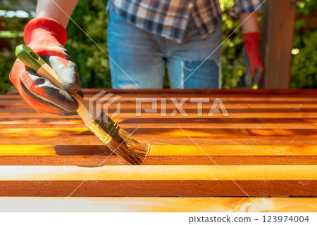 Close-up of a worker's hand applying wood stain with a paintbrush on wooden beams Close-up of a worker's hand applying wood stain with a paintbrush on wooden beams 123974004
