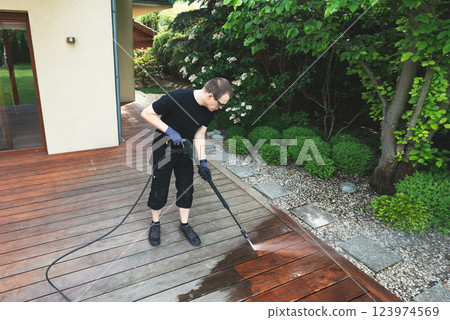 man cleaning terrace with a power washer - high water pressure cleaner on wooden terrace surface man cleaning terrace with a power washer - high water pressure cleaner on wooden terrace surface 123974569