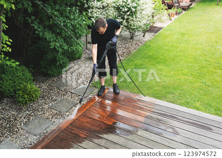 man cleaning terrace with a power washer - high water pressure cleaner on wooden terrace surface 123974572