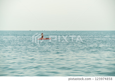 Paddleboarder Gliding Over Calm Water During a Serene Daytime Adventure Paddleboarder Gliding Over Calm Water During a Serene Daytime Adventure 123974858