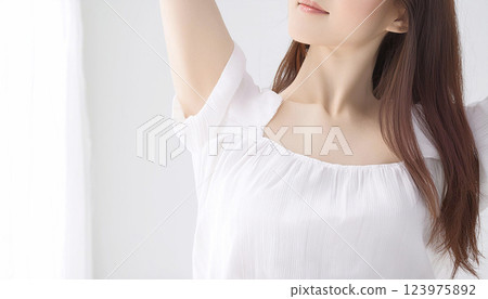 一名身穿白色衣服的女子正以白色房間的牆壁為背景進行伸展運動。 123975892