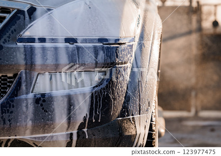 Close-up View of a Car Front Being Washed with Soap and Water Outdoors at Sunset Close-up View of a Car Front Being Washed with Soap and Water Outdoors at Sunset 123977475