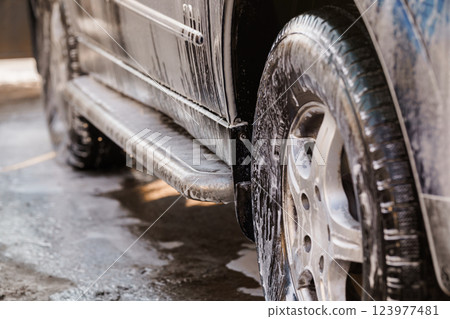 Close-Up of Car Wheel and Side Step Covered in Soap Foam During Vehicle Wash 123977481