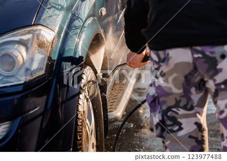 Person Washing Car Wheel Using Pressure Washer on Sunny Day 123977488
