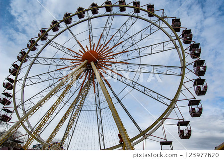 Entertainment attraction Ferris wheel. A non-working Ferris wheel rotates smoothly in the wind against a cloudy sky. 123977620