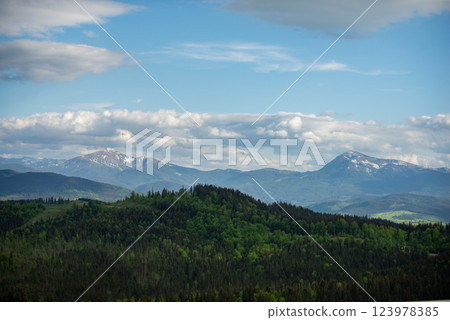 Expansive mountain landscape showcases lush greenery and distant peaks under a partly cloudy sky in early spring light 123978385
