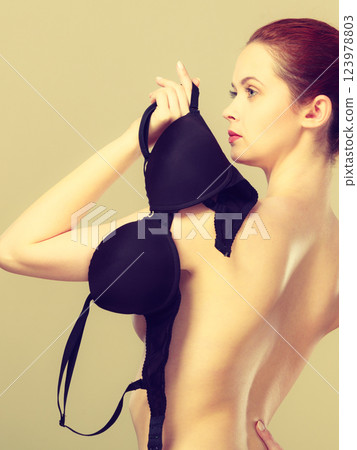 Naked woman holds black bra in hand 123978803