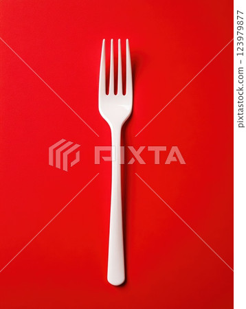 Close-up of a white plastic fork against vibrant red backdrop 123979877