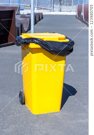 Covered yellow plastic garbage container with wheels on the street Covered yellow plastic garbage container with wheels on the street 123980705
