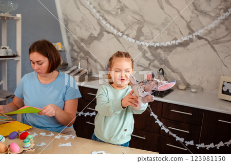 Mid shot of young mother and happy little girl play with rabbit glove, sitting at Easter table. Spring holiday 123981150