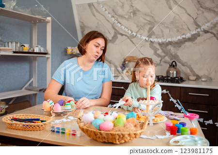 Wide shot of mother and her child sitting at the festive table for Easter and prepares decorations 123981175